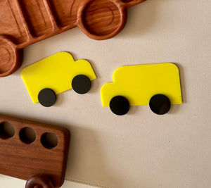 Two bright yellow toy truck shapes with separate round black wheels on a beige textured background