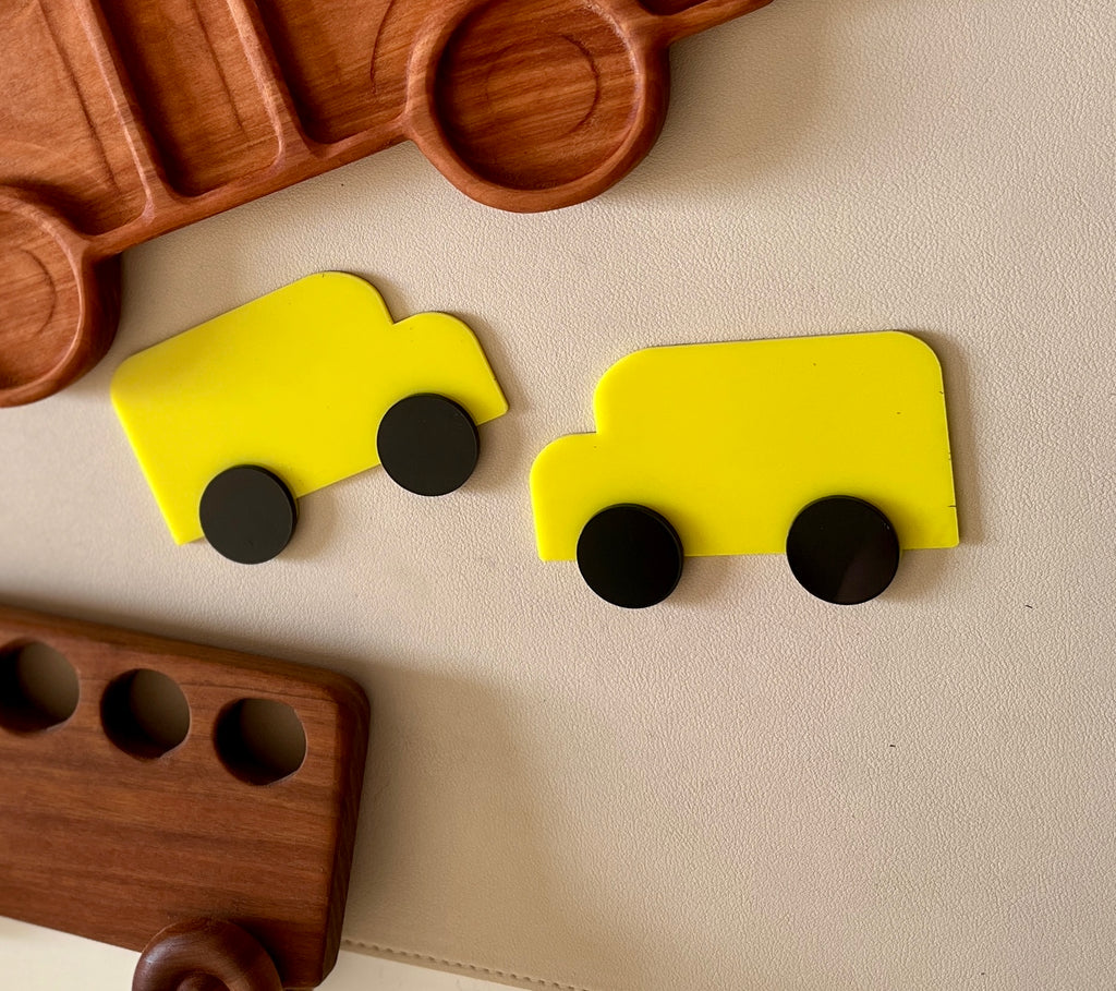 Two bright yellow toy truck shapes with separate round black wheels on a beige textured background
