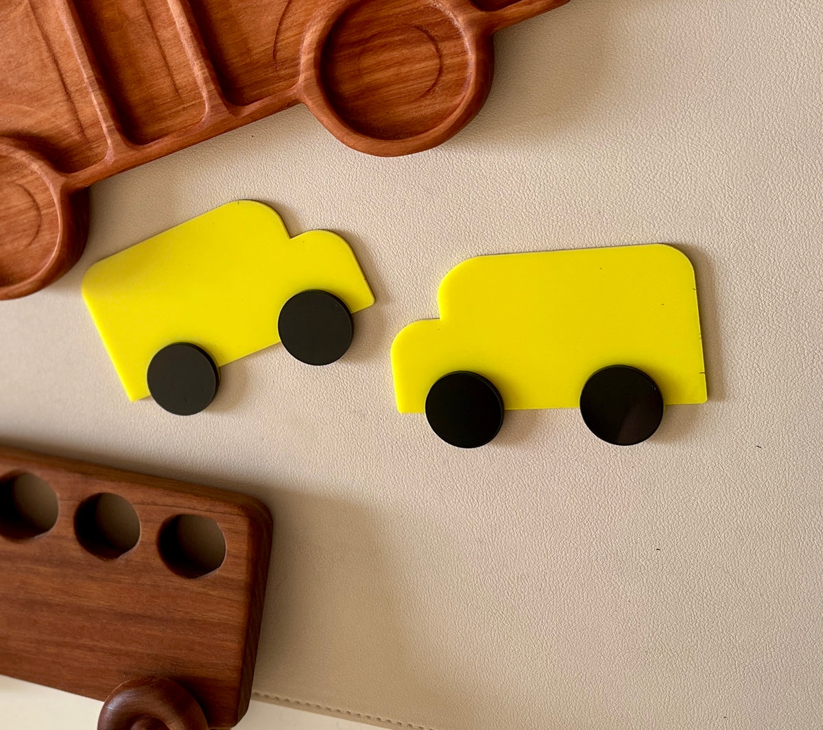 Two bright yellow toy truck shapes with separate round black wheels on a beige textured background