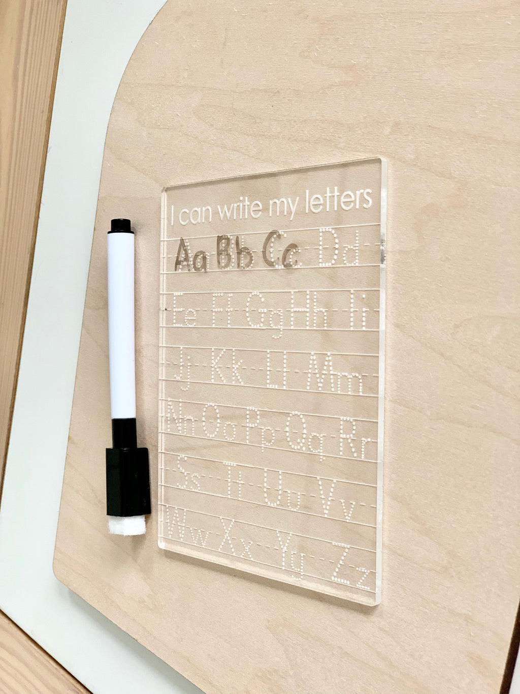 Clear acrylic letter tracing board with uppercase and lowercase alphabet and a black dry erase marker on wooden surface