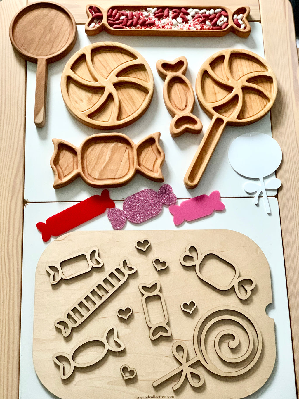 Wooden trays shaped like candies and lollipops with red and white beans, colorful paper cutouts, and small hearts on light background