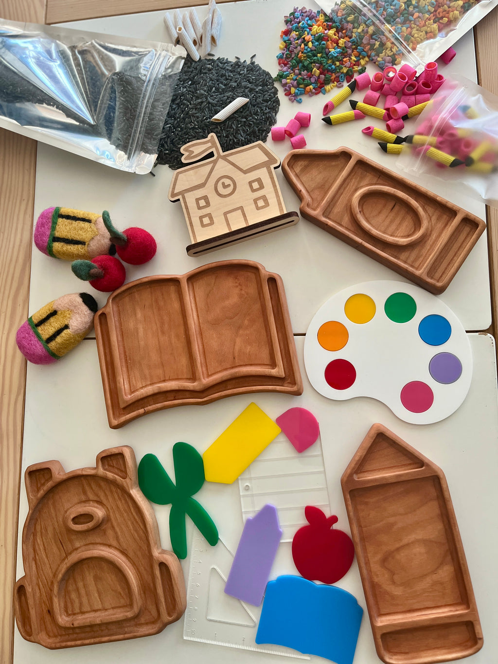 Carved wooden trays in shapes of schoolhouse, backpack, book, pencil, and paint palette with colorful craft supplies scattered around