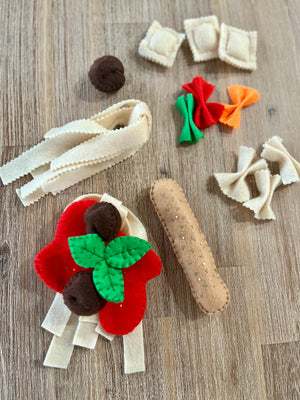 Various felt pasta shapes including beige noodles, red and orange farfalle, ravioli, meatballs, and a baguette, arranged on a wooden surface, Felt Pasta Set, Made in Canada, handcrafted, homeschool, education resources.