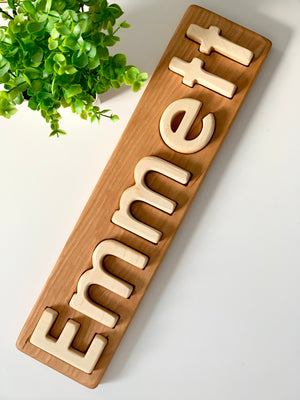 Personalized hardwood name puzzle with light wooden letters spelling Emmett on natural wood board next to green plant