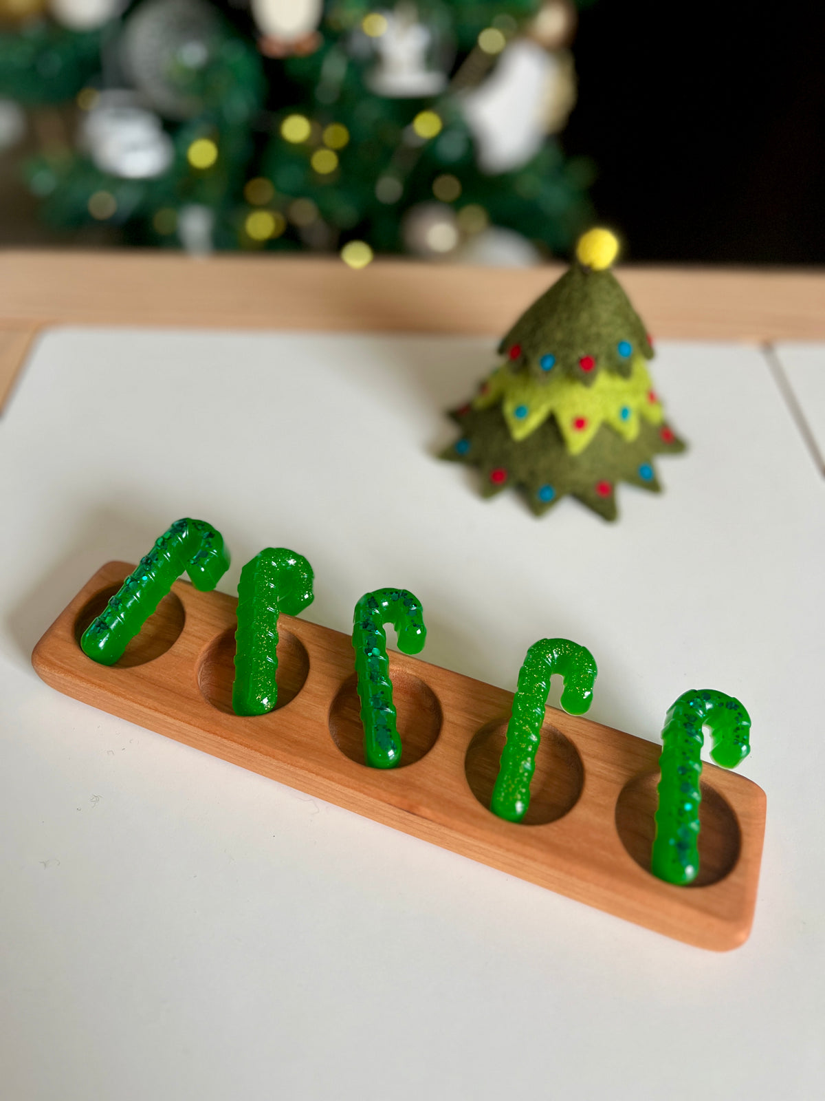Wooden tray holding five green gummy candy canes with a green felt Christmas tree decoration in the background