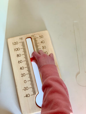 Child’s hand adjusting red indicator on wooden thermometer with Fahrenheit and Celsius scales on light surface