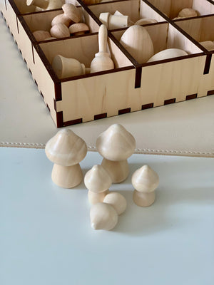 Five smooth unfinished wooden mushroom shapes displayed in front of a sectioned wooden storage box containing more wooden pieces