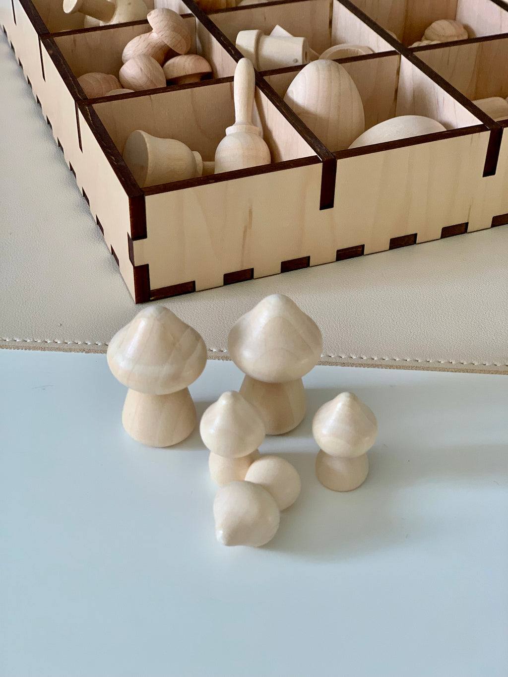 Five smooth unfinished wooden mushroom shapes displayed in front of a sectioned wooden storage box containing more wooden pieces
