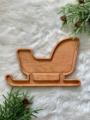 Wooden sled-shaped sensory tray with natural wood grain on white faux fur background with pine branches and pinecones