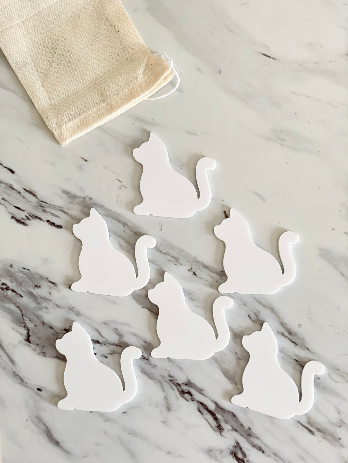 Set of six white dry erase cat-shaped pieces with a small cloth drawstring bag on marble surface