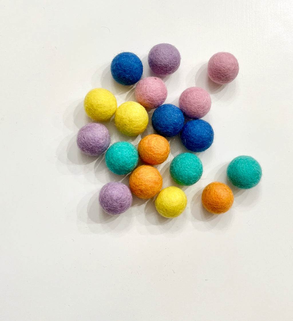Cluster of colorful felt balls in yellow, purple, pink, blue, orange, and teal scattered on a white background