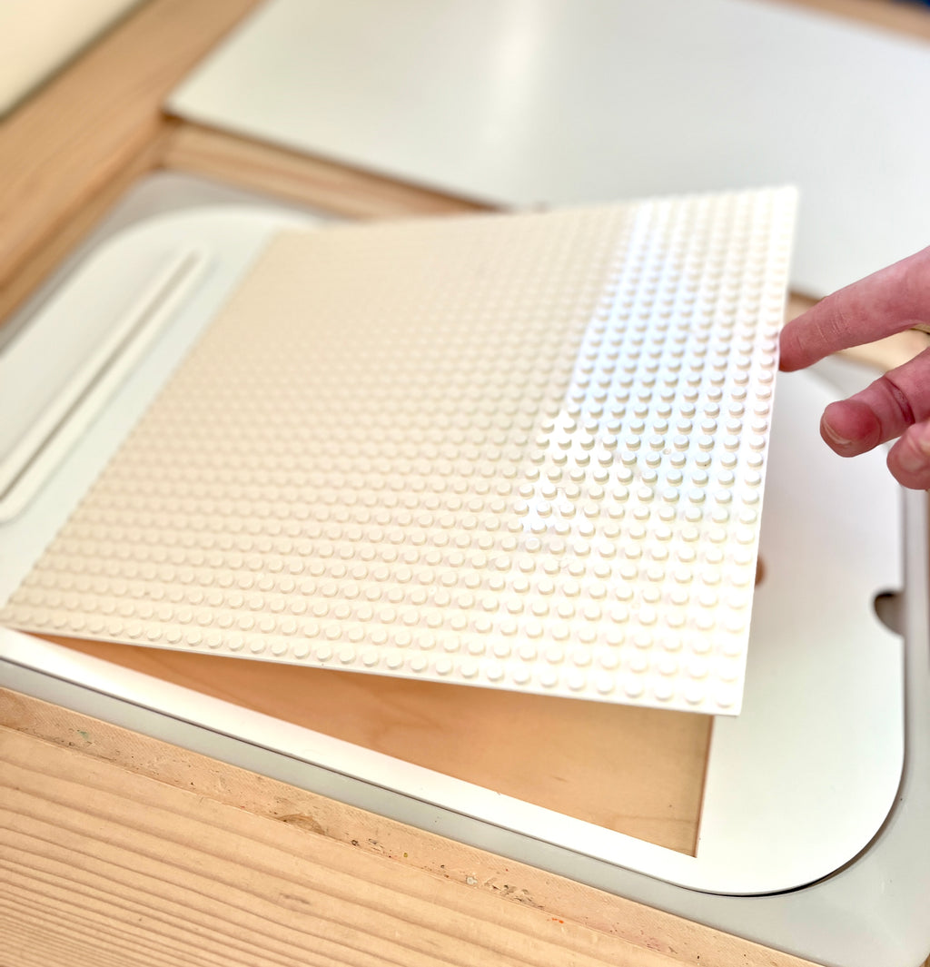 Hand lifting a white pegboard panel above a recessed compartment on a light wooden surface