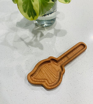 Small wooden scoop-shaped tray with smooth grooves placed on white countertop near glass vase with green leaves