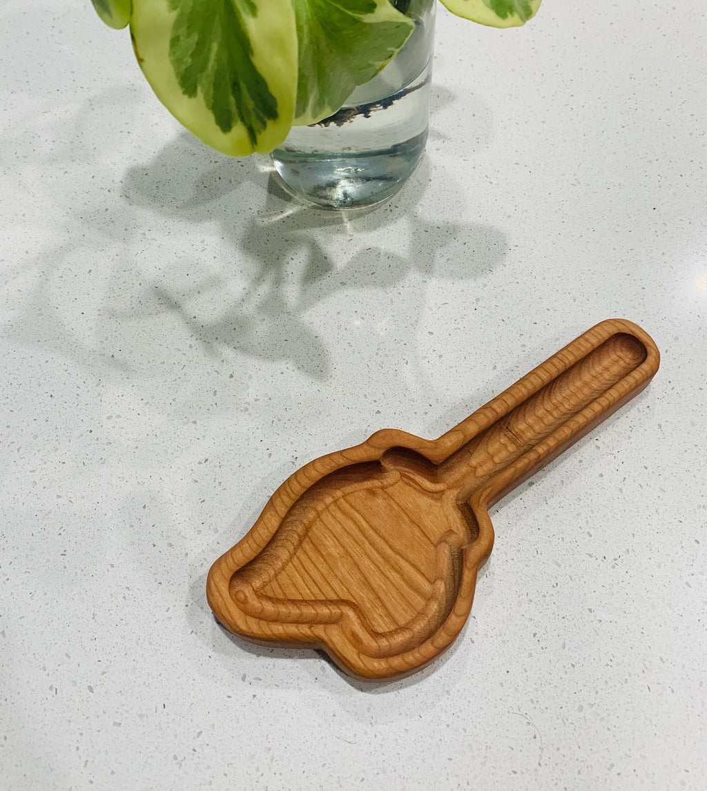 Small wooden scoop-shaped tray with smooth grooves placed on white countertop near glass vase with green leaves