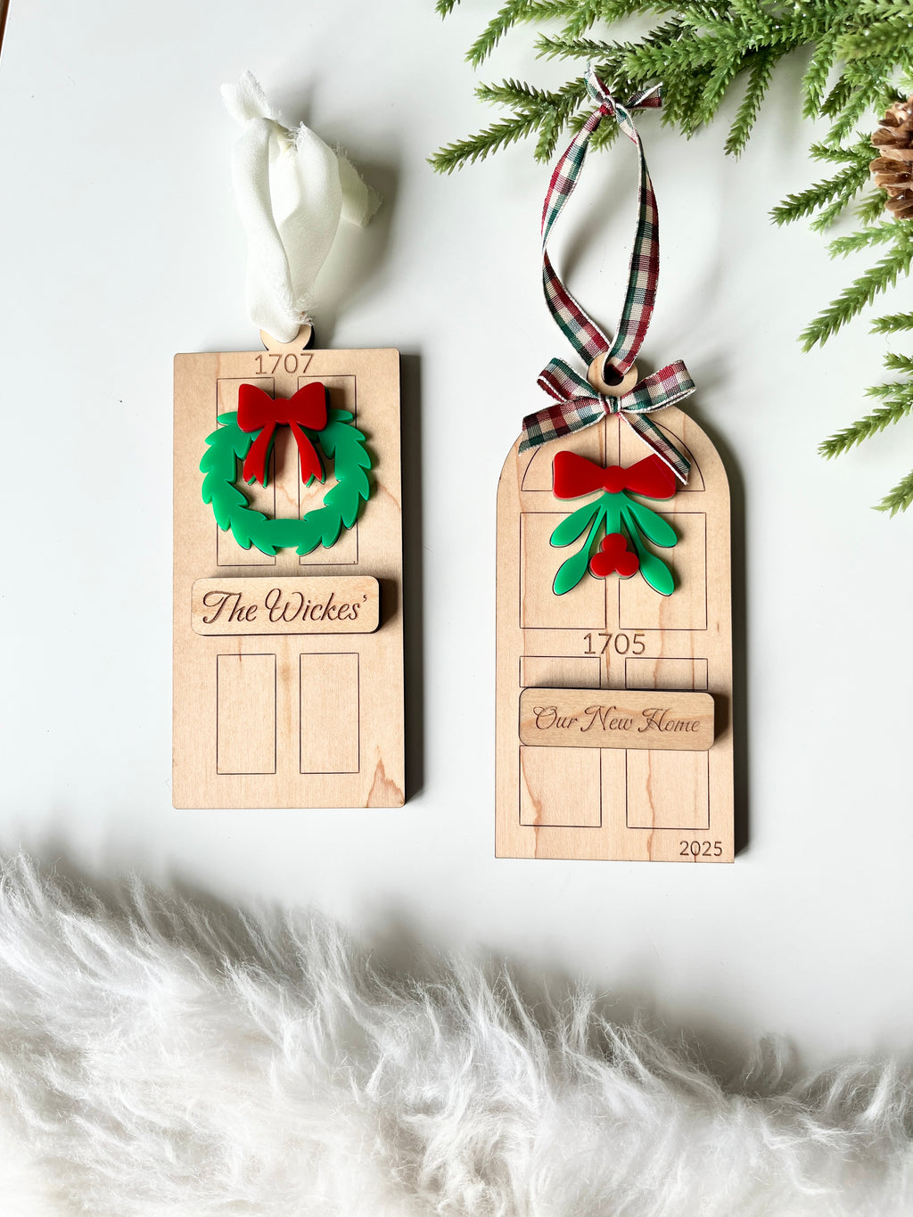 Two wooden door-shaped ornaments featuring green wreaths, red bows, personalized plaques, and fabric ribbons on white background