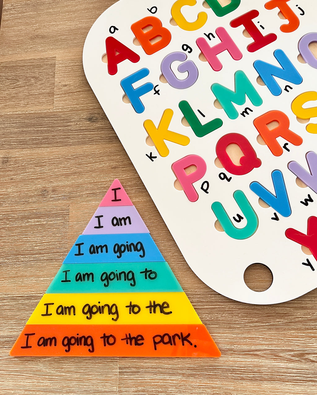 Little Dry Erasable Sentence Building Pyramid; Fluency Triangle with colorful layered pieces showing progressive sentence building on wood surface alongside a white board with colorful uppercase alphabet letters, handcrafted homeschool education resources.