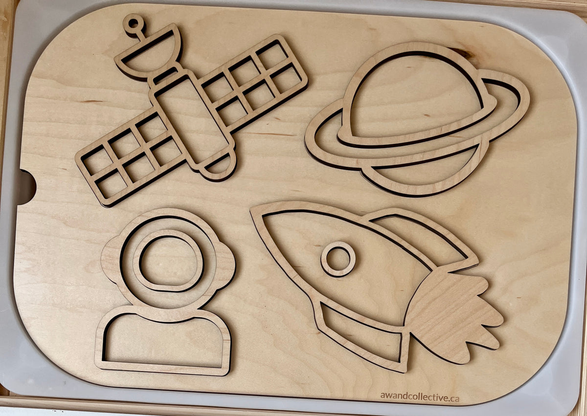 Wooden puzzle board with cutouts of a satellite, planet with rings, astronaut helmet, and rocket ship outlines.
