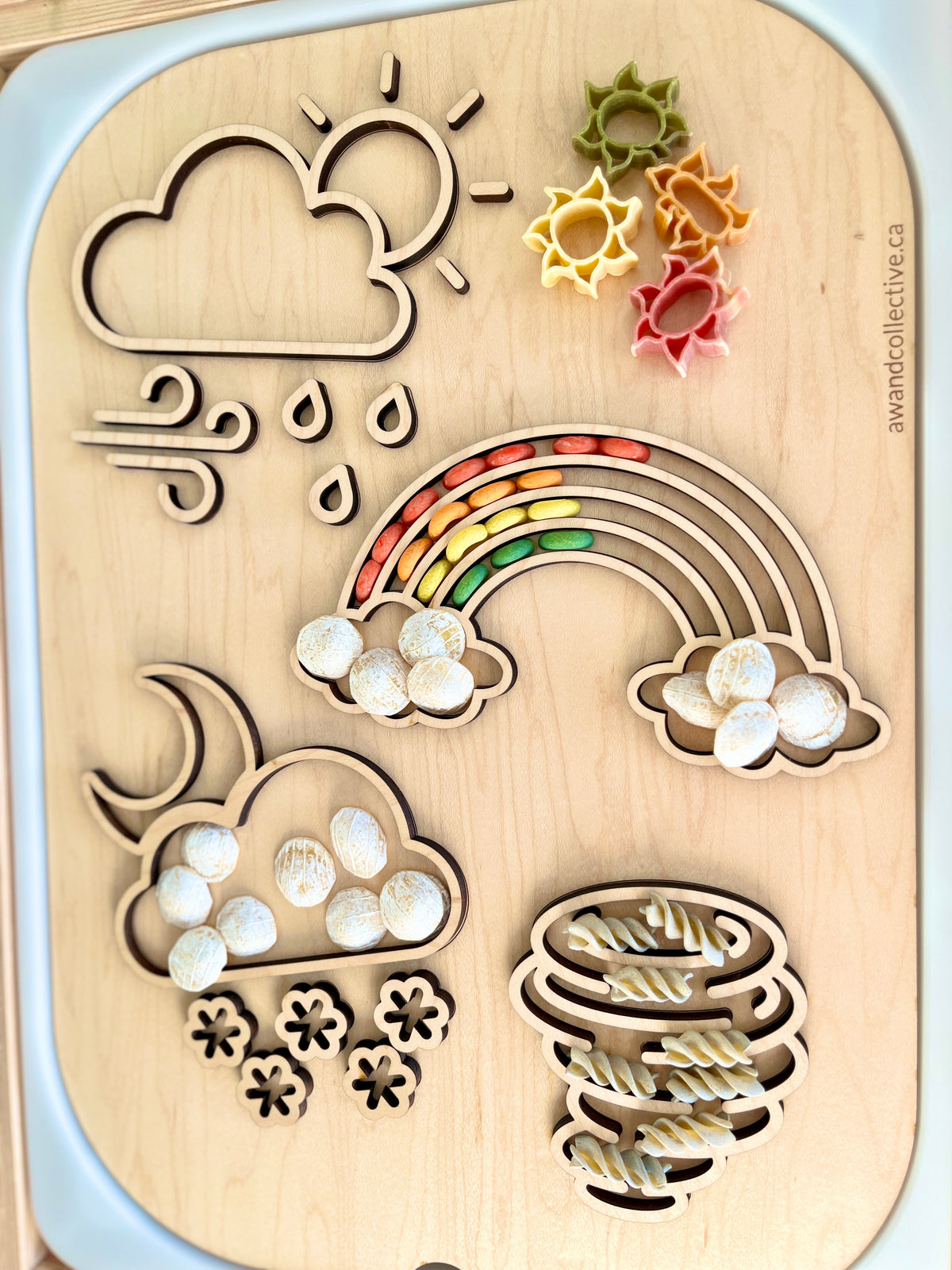 Wooden weather-themed puzzle board with sun, cloud, raindrops, snowflakes, rainbow, and spiral shapes filled with colorful beads and pasta pieces