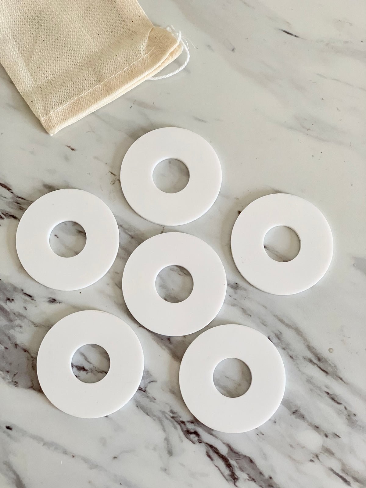 Set of six white donut-shaped little dry erasable discs arranged on marble surface with cloth drawstring bag nearby