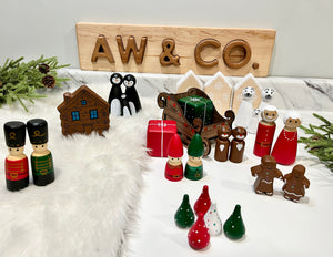 Wooden holiday figurines including soldiers, gnomes, gingerbread people, penguins, polar bears, sleigh, gift box, and houses on marble surface