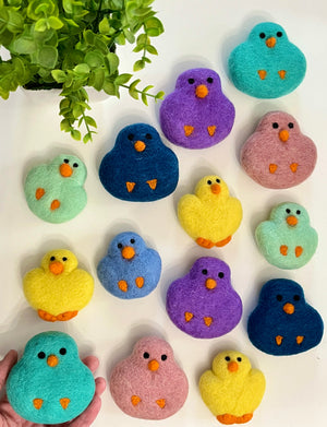 Colorful felt bird-shaped decorations in shades of yellow, purple, blue, pink, and teal arranged on white surface next to plant leaves