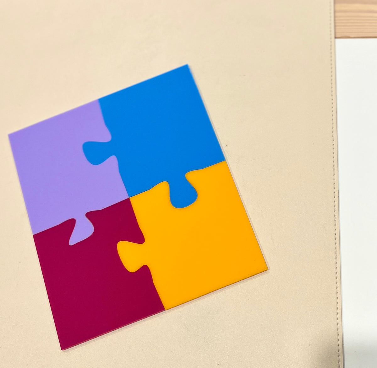 Four connected puzzle pieces in purple, blue, yellow, and dark red on a light beige surface