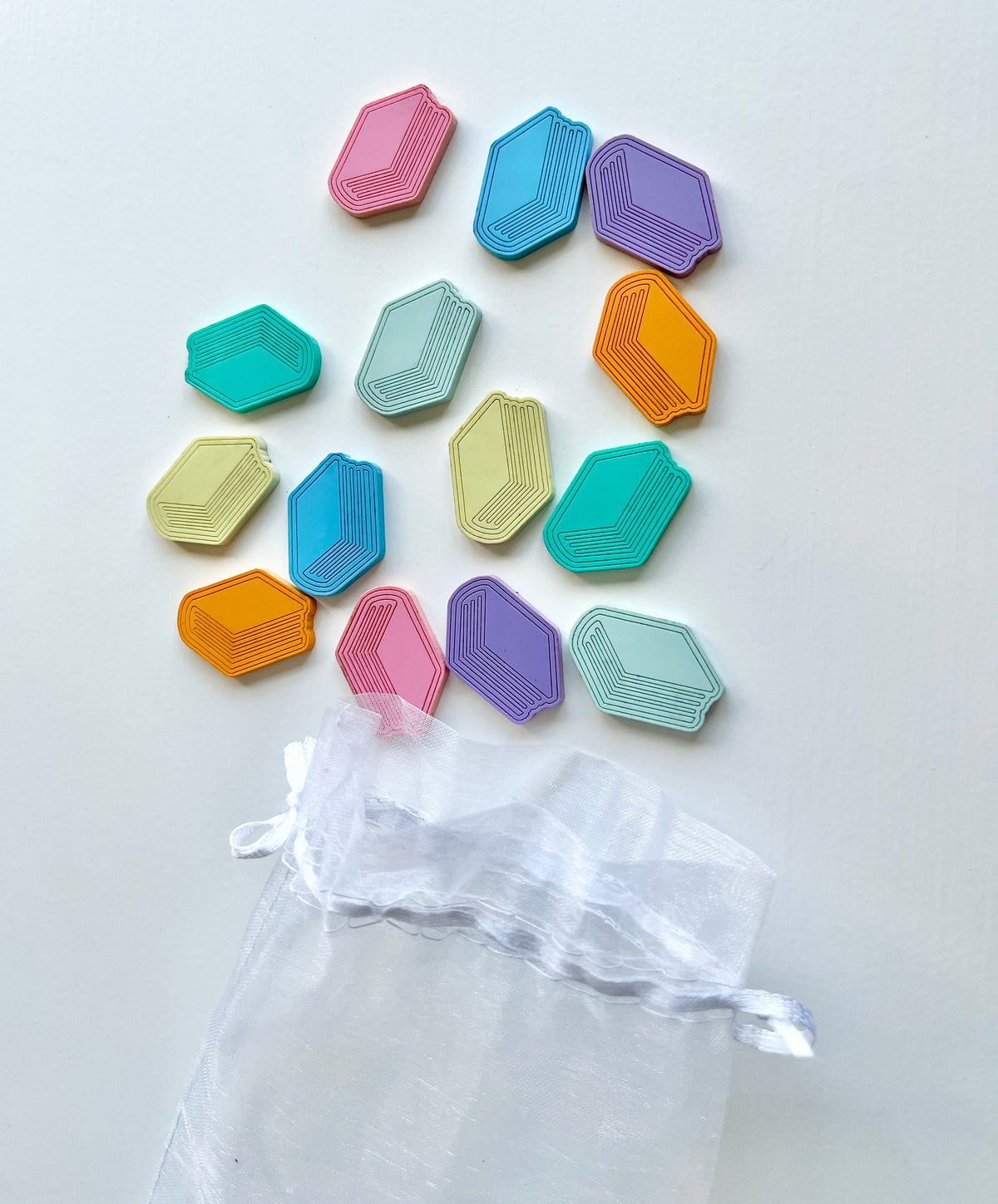 Multicolored geometric game tokens scattered above a translucent white drawstring pouch on a white background