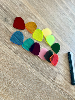 Ten translucent gum drop pieces in various colors arranged on a wood surface next to a black and white dry erase marker, showcasing Little Dry Erasables — Set of 10 Translucent Gum Drops with handcrafted homeschool education resources.