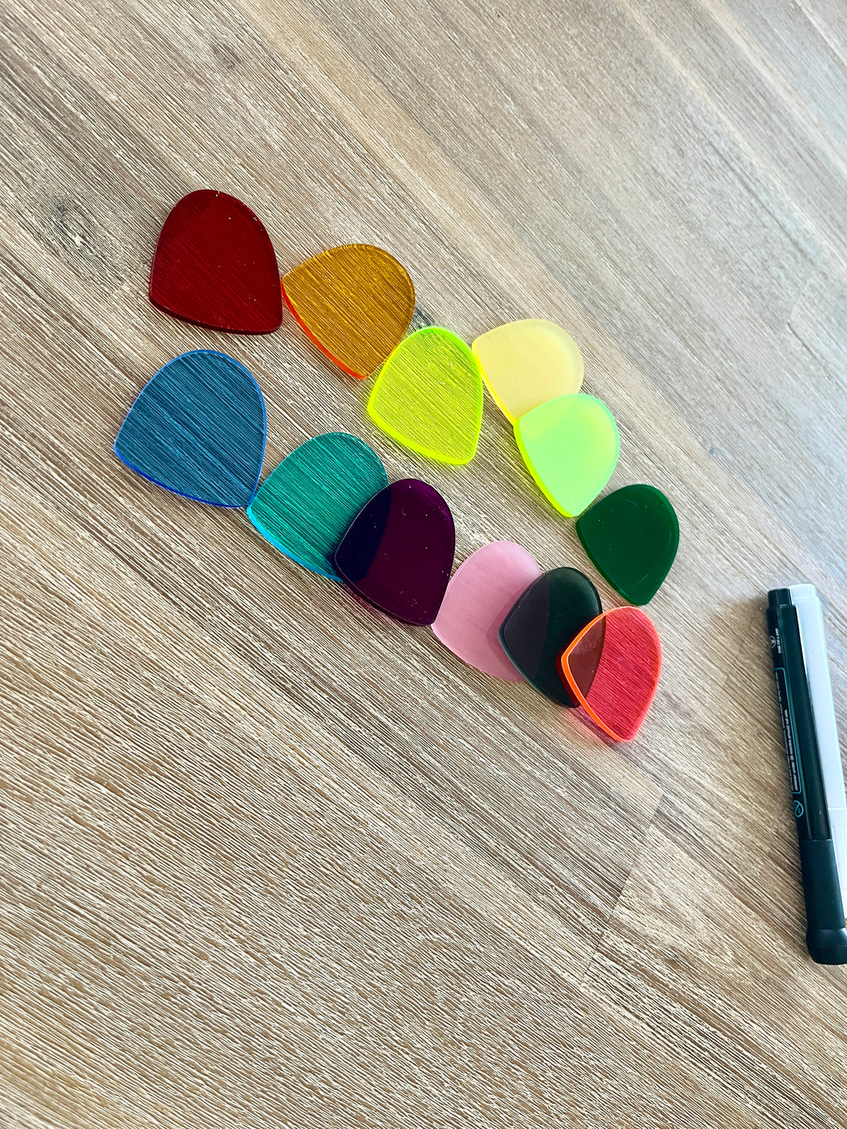 Ten translucent gum drop pieces in various colors arranged on a wood surface next to a black and white dry erase marker, showcasing Little Dry Erasables — Set of 10 Translucent Gum Drops with handcrafted homeschool education resources.
