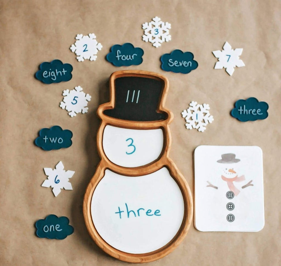 Snow person sensory tray with numbered snowflake and cloud pieces and matching snowman counting card on brown background
