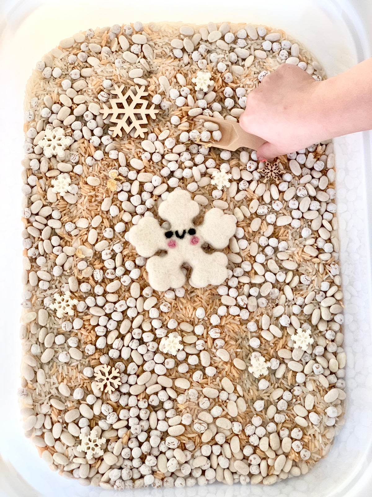 Winter sensory bin filled with white beans, rice, wooden snowflakes, and a felt snowflake with a wooden spoon handSubview