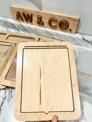 Light wooden tray with a rectangular groove held above other trays on a marble-patterned surface under a wooden AW & CO sign