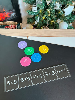 Black writing surface with multiplication problems in white squares and colorful round discs displaying answers nearby