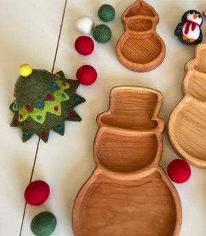 Wooden snowman-shaped trays with felt red, green, and white balls and a decorated felt Christmas tree on white surface