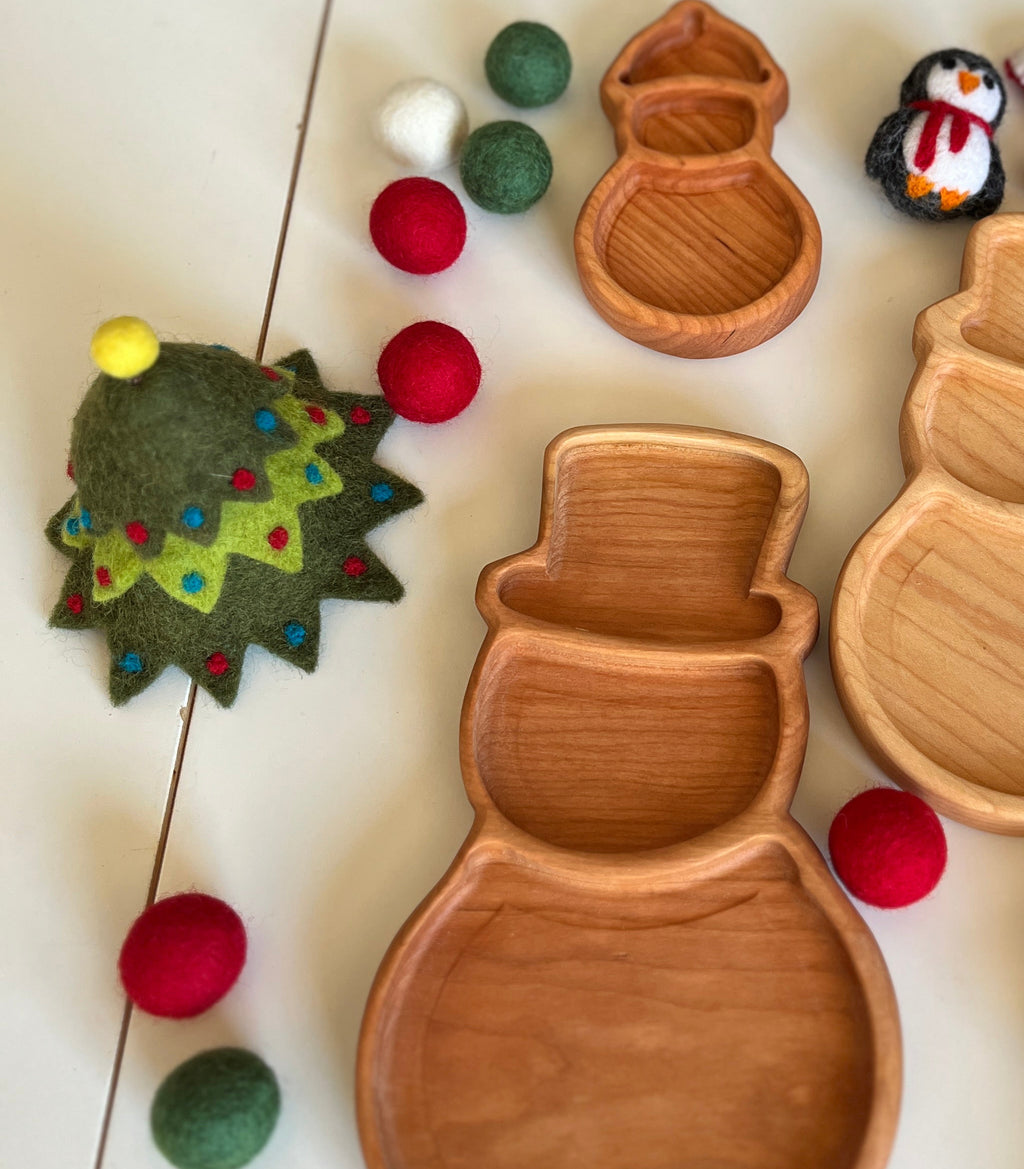 Wooden snowman-shaped trays with felt red, green, and white balls and a decorated felt Christmas tree on white surface