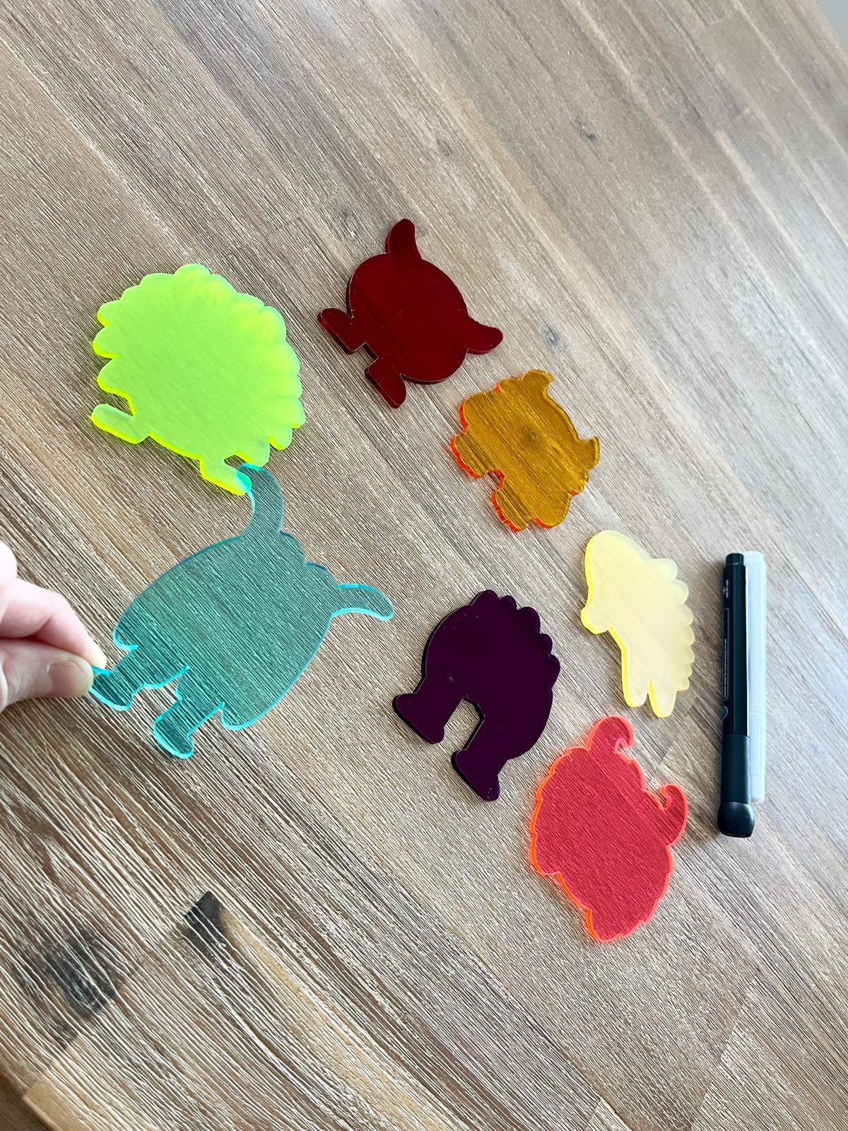 Collection of colorful translucent monster-shaped pieces arranged on a wooden surface with a dry erase marker nearby, highlighting Little Dry Erasables — Translucent Monsters Set of 7, handcrafted homeschool education resources.