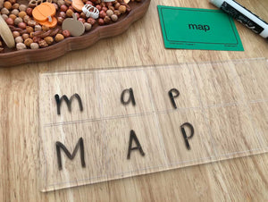 Transparent board with lowercase and uppercase letters m, a, p arranged in columns beside a green word card and dry erase marker