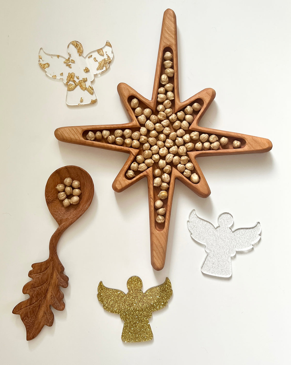 Wooden star-shaped tray filled with hazelnuts surrounded by wooden spoon and decorative angel cutouts on white surface