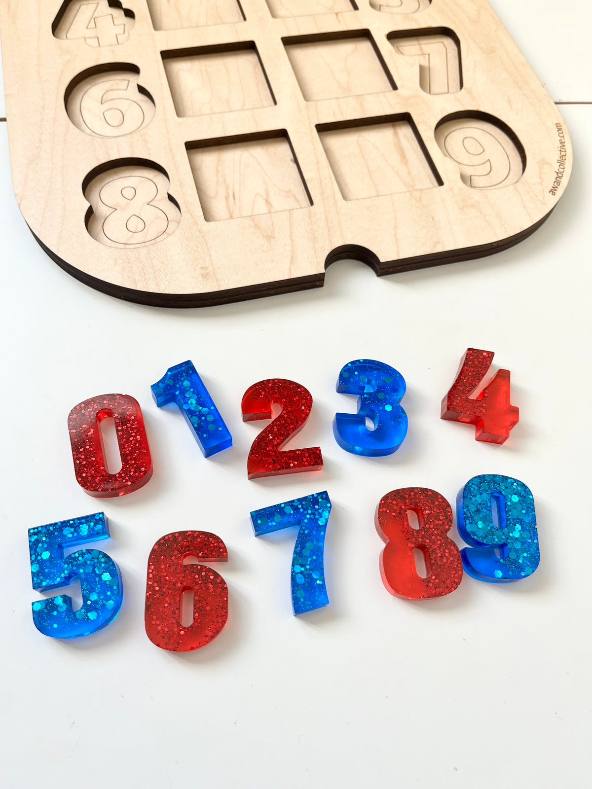 Glitter-filled red and blue resin numbers zero through nine displayed near a wooden number puzzle board