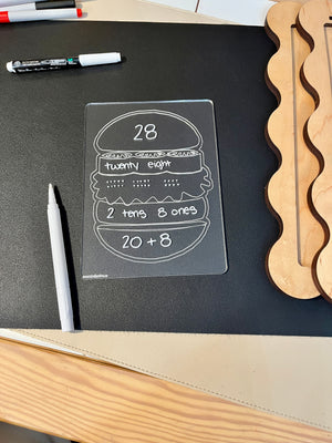 Clear plastic board with number 28 represented as digits, words, place value, and addition on a black surface with markers nearby