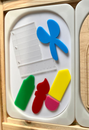 Translucent plastic shapes resembling a fan and measuring tools alongside solid green, red, yellow, and pink geometric pieces on a white tray