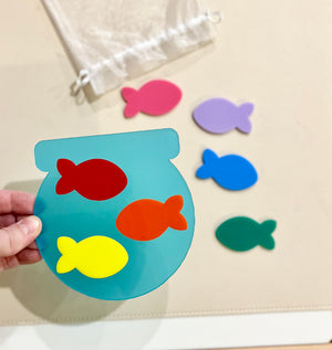 Translucent blue fishbowl-shaped cutout with red, orange, and yellow fish, surrounded by separate pink, purple, blue, and green fish pieces