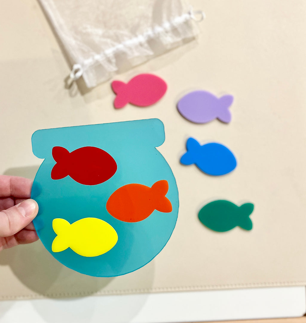 Translucent blue fishbowl-shaped cutout with red, orange, and yellow fish, surrounded by separate pink, purple, blue, and green fish pieces