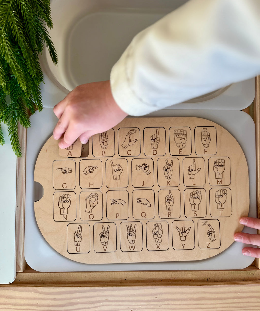 Child’s hand placing a puzzle piece on a maple wood ASL alphabet Flisat insert tabletop with sign illustrations