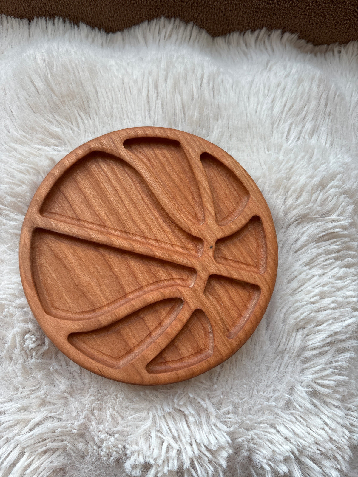 Round wooden tray carved with basketball-inspired grooves on a soft white textured fabric surface