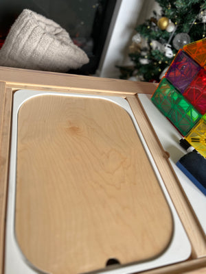 Light wooden serving tray with rounded edges inside a wooden box with colorful translucent magnetic tiles nearby