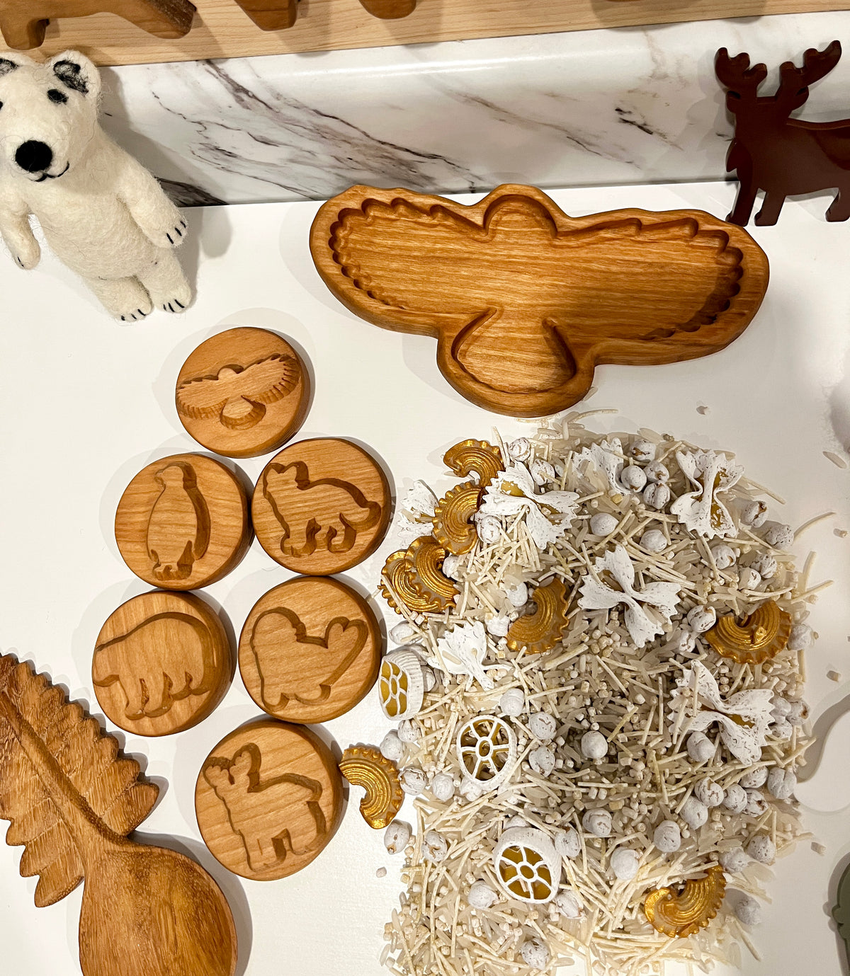Wooden bird-shaped dish, round wooden animal stamps, felt polar bear, moose figure, and natural sensory materials on white surface
