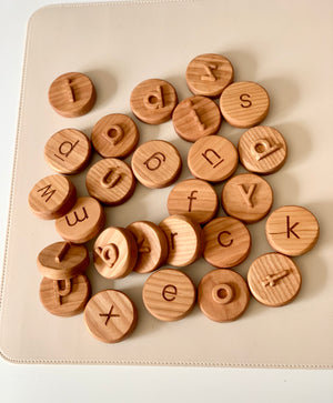 Scattered round wooden tokens engraved with lowercase and uppercase letters on a light beige surface