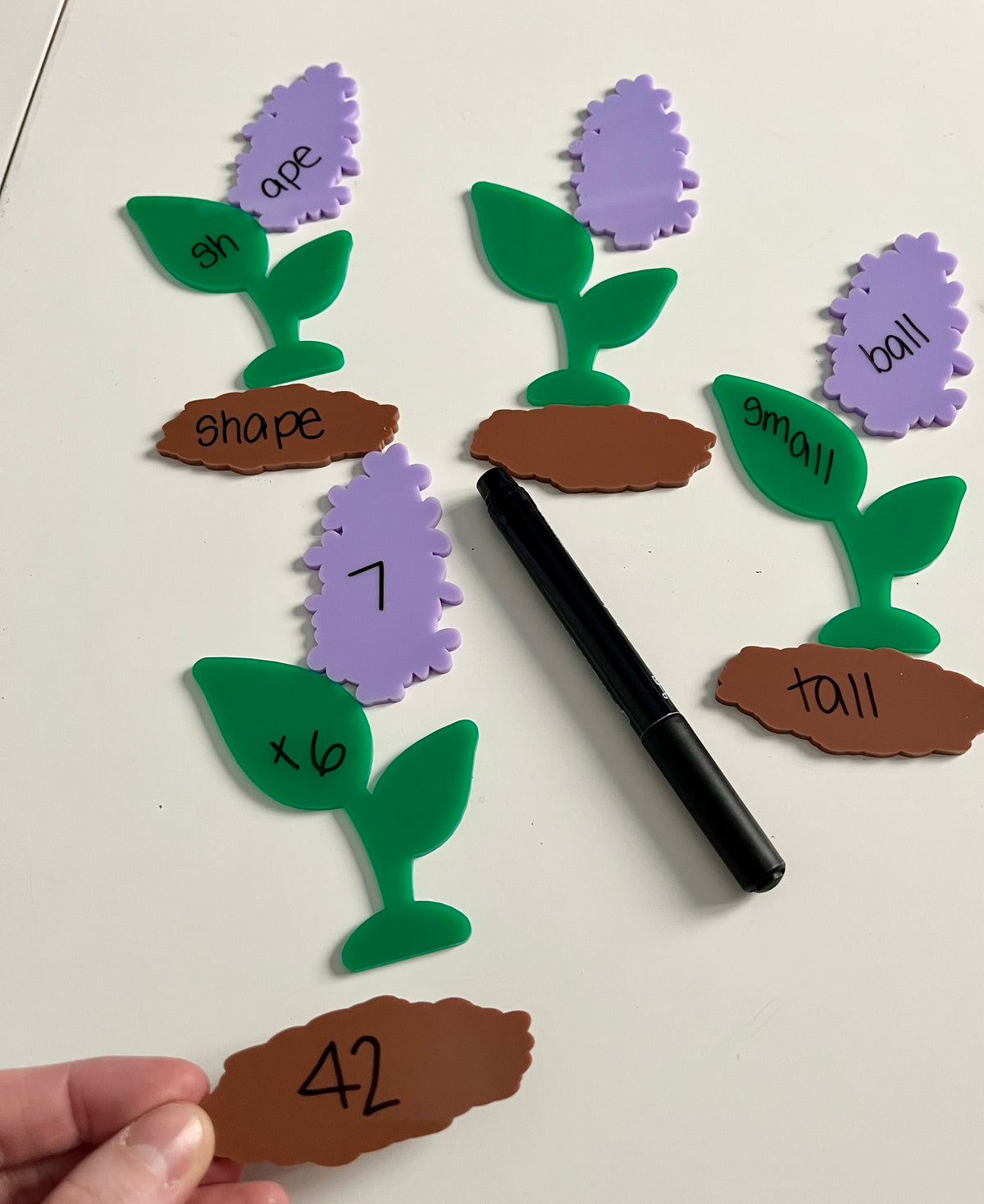 Little Dry Erasables - 3 Part Lavender with Soil Flowers showing purple flower pieces, green leaves, and brown soil segments with handwritten words and numbers, black dry erase marker, handcrafted homeschool education resources.
