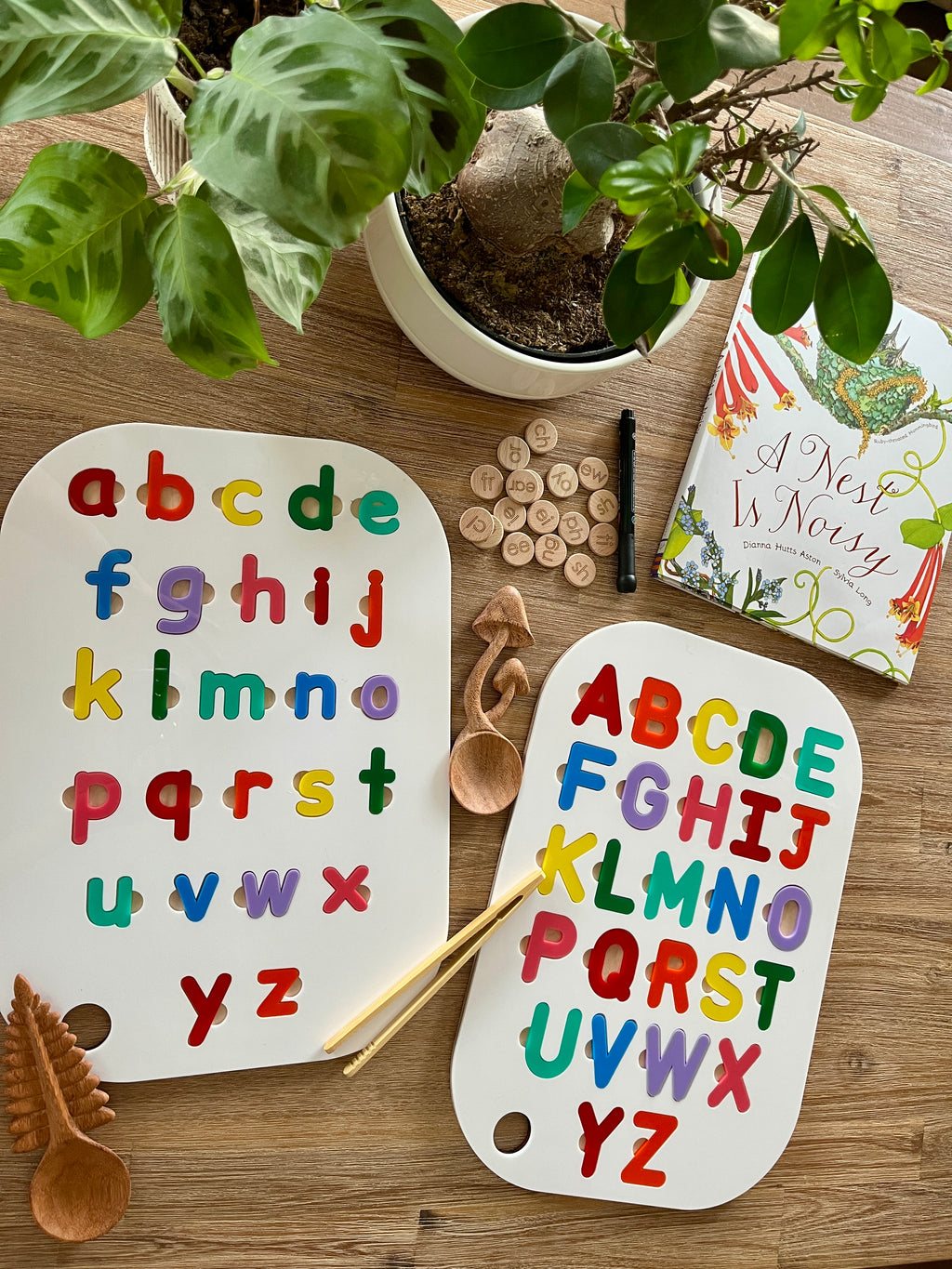 Acrylic Dry Erase Lowercase Alphabet Puzzle Flisat Table Top Insert with Both Rainbow and White Letters displayed alongside wooden scoops, letter discs, a pen, and a nature-themed book, featuring handcrafted homeschool education resources.
